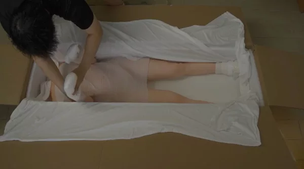 Slide your hands under the doll’s upper arms and gently lift them up and out of the foam cradle.